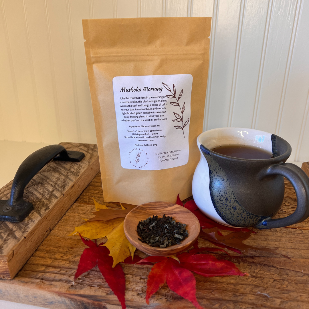 Package of loose leaf tea called Muskoka Morning on a try with a brewed cup of tea, a small saucer of loose tea and maple leaves.