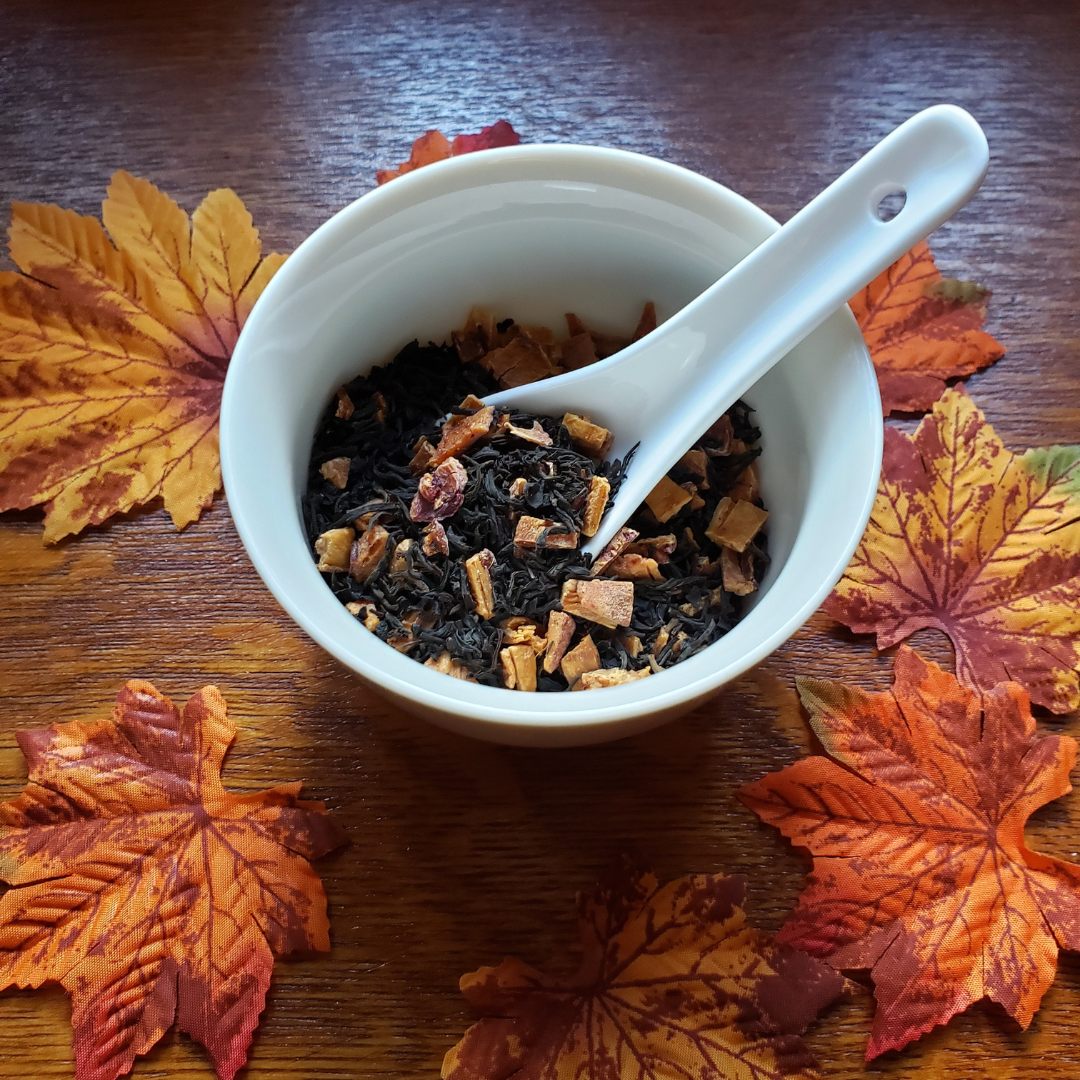 Loose leaf black tea stirred with dried peach pieces in a cup with spoon on background of wooden tray with maple leaves