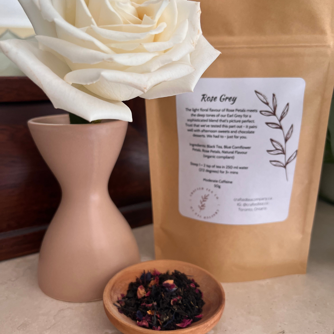 Package of Rose Earl Grey Tea beside a rose bud in a vase.  A small tray of the loose leaf tea with rose petals sits in front